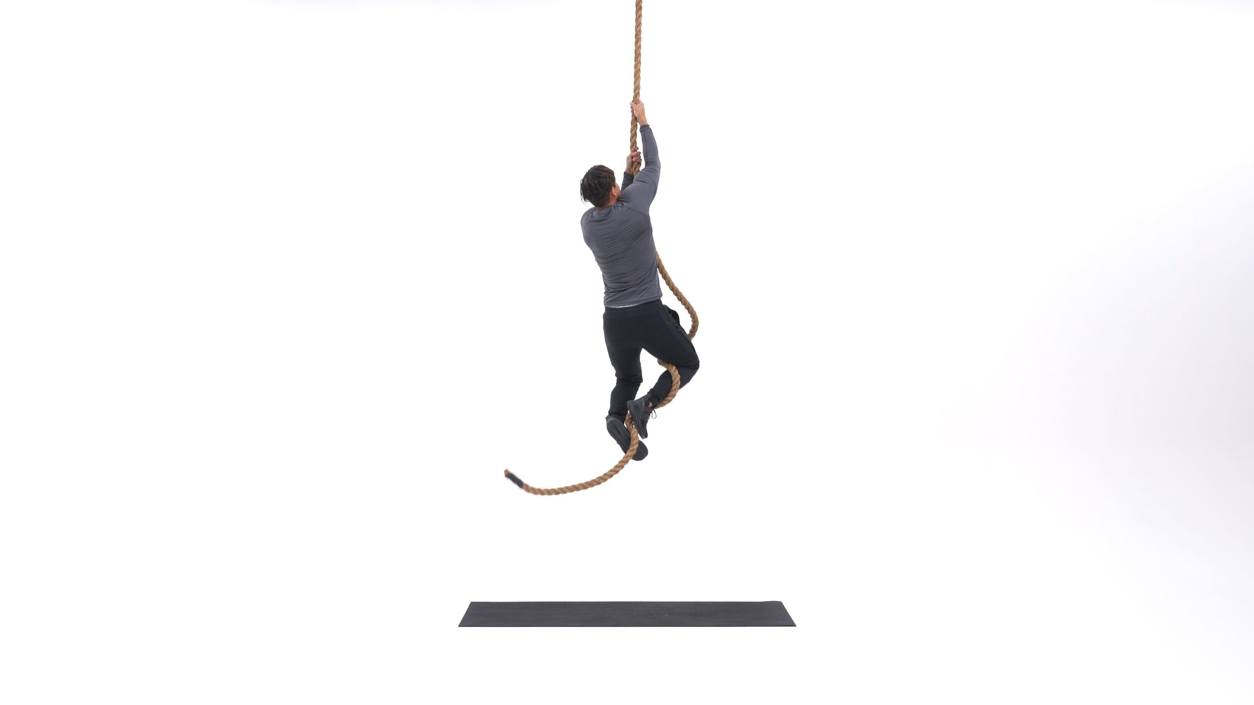 فرد در حال بالا رفتن از طناب، با دستانی که طناب را محکم گرفته و بدنش در حال حرکت به سمت بالا است.